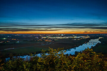 Sonnenuntergang &uuml;ber der Stadt mit Fluss und l&auml;ndlicher Umgebung am Abend