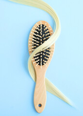 A lock of blonde hair, hair care products and a comb on a colored background. Vertical photo format