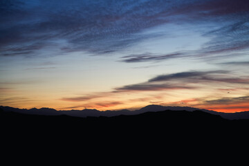 Sunset landscape with colorful sky and mountains in silhouette under evening light and clouds