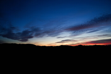 Dark blue sky after sunset with red horizon glow and soft moving clouds over distant hills