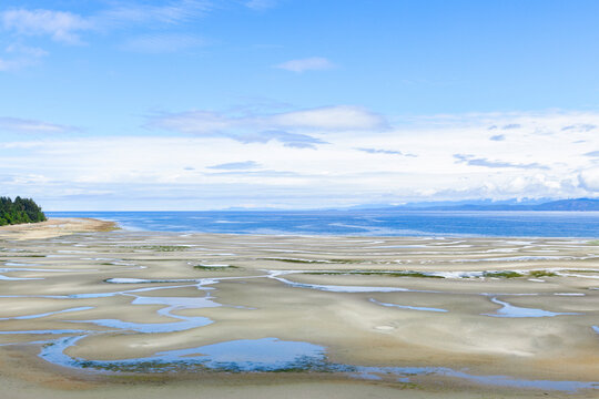 Panoramic view to the sandy beach with tide pools at low tide, blue sky with white clouds in summer day. Parksville, Vancouver island, BC, Canada.