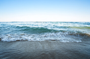 Ocean waves rolling on sandy beach under clear blue sky