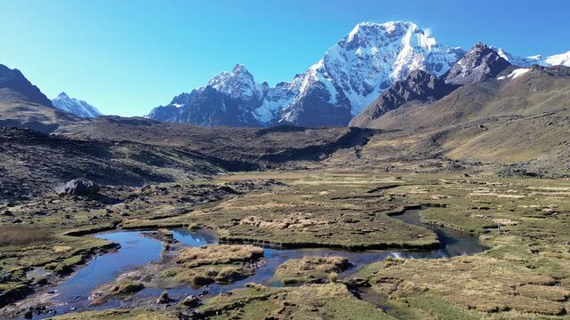 Ausangate, Peru: Orbit aerial drone footage on a river heading to Ausangate, a mountain in Andes, Peru, showing the 6,384 metres peak under a clear blue sky in early morning. 