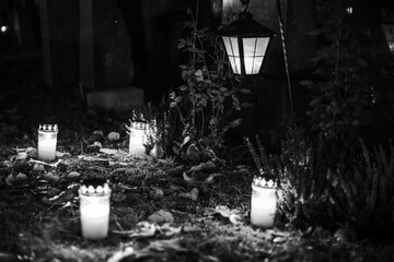 Black and white photograph of cemetery crosses and glowing lanterns, soft candlelight creating a...