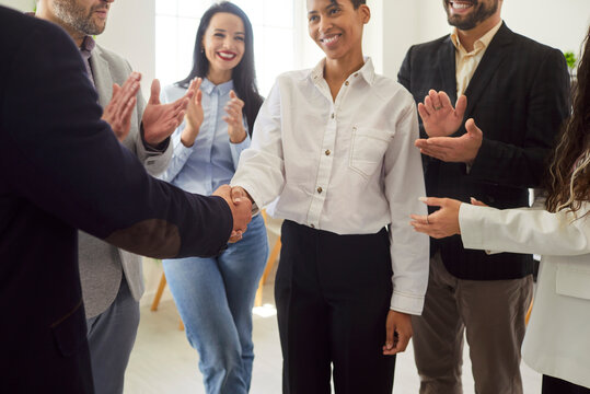Handshake between corporate leader and happy businesswoman amidst applause from colleagues. Best employee and boss shake hands on event, people applaud with smiles and respect. Recognition concept - Powered by Adobe