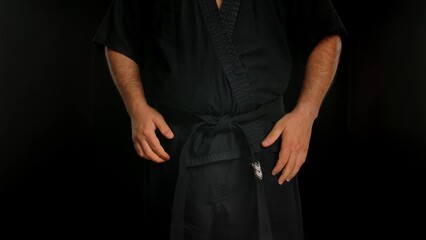 A martial arts master in a traditional black kimono stands against a black background. The man is...