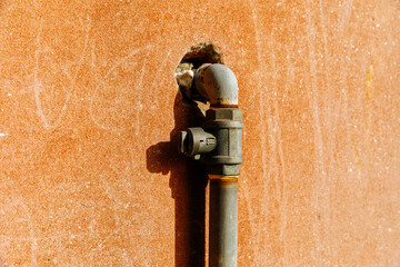 Rusty metal wall with industrial pipe fixture in bright sunlight