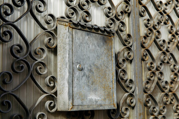 Rustic mailbox on ornate iron gate with intricate swirl design