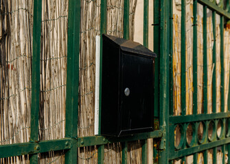Black mailbox attached to green metal fence with bamboo panels
