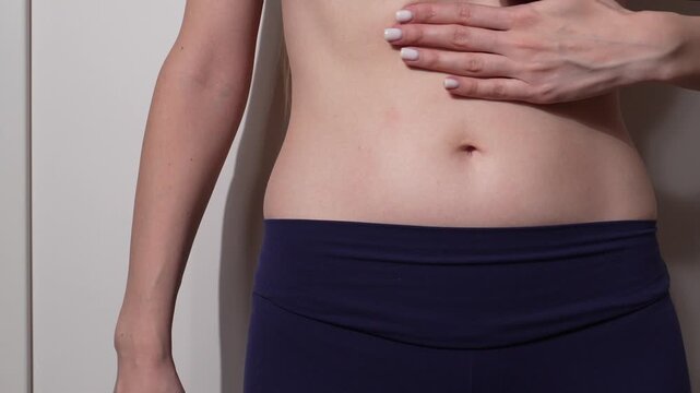 Close-up of woman touching her flat stomach in blue leggings indoors. Concept of body care, self confidence, wellness, healthy lifestyle and natural beauty. Minimalist and clean look.
