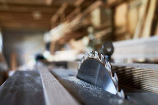 Close up showing circular saw blade cutting wooden plank in carpentry workshop, sharp metal teeth visible with blurred background emphasizing woodworking process and industrial equipment