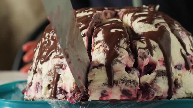 Slicing chocolate volcano berry cake - homemade Pancho cake, showing the white sour cream frosting, berries, and chocolate drizzle