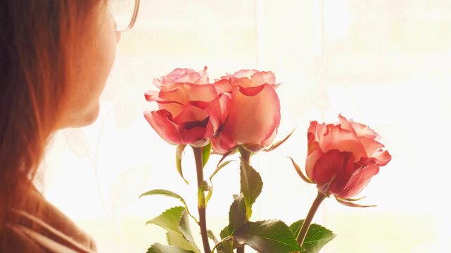 Romantic shot of a woman appreciating the aroma of fresh pink roses near the window