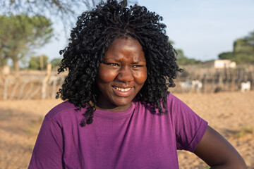 Fototapeta premium young african woman, in the village, at the farm in the yard, goats in the pen, sandy ground