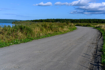 Winding dirt road leading to a serene lakeshore under a bright blue sky