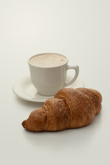 A cup of coffee with a croissant on a milky beige background
