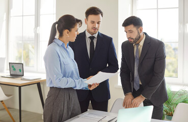 Portrait of three business people standing in office near the workplace looking through financial...