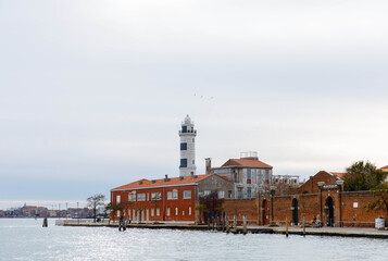  Scenic view of Murano Island featuring historic lighthouse and colorful buildings along the waterfront, capturing the charm of Venetian architecture and coastal beauty