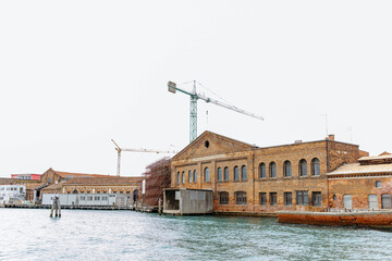 Murano, Italy - November 21, 2024: Scenic view of historic Murano island architecture with waterfront, showcasing traditional buildings and modern cranes, reflecting the blend of history and progress
