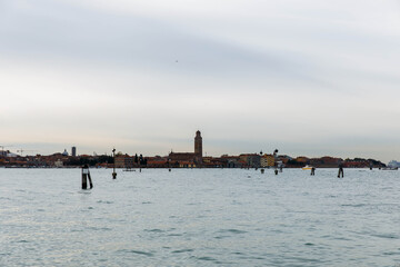 Murano, Italy - November 21, 2024: Scenic view of Murano Island with historic buildings and bell tower reflected in calm waters, showcasing the beauty of Venetian architecture and serene atmosphere