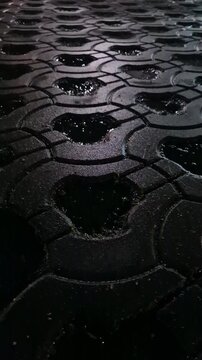 Puddles pavement night, wet interlocking brick surface texture glistening in the low light after heavy rain