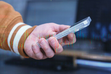 Hand holding a modern smartphone over an abstract digital background featuring financial data, stock market quotes and a glowing candlestick chart overlay.