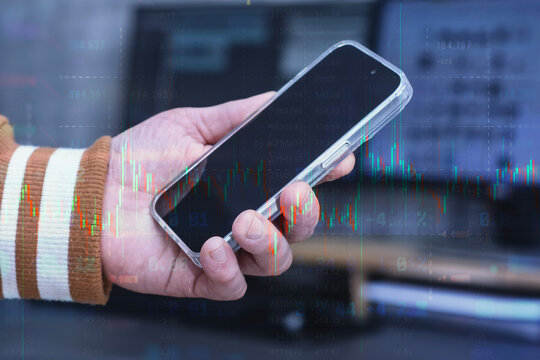 Hand holding a modern smartphone over an abstract digital background featuring financial data, stock market quotes and a glowing candlestick chart overlay.