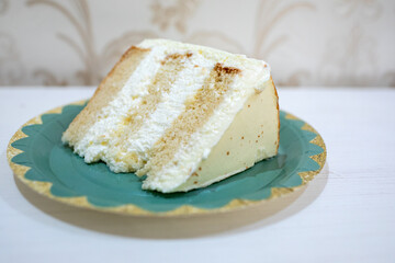 Single slice of layered vanilla sponge cake with rich white cream frosting on a teal and gold decorative paper plate