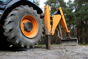 A tractor with an excavator mechanism digs a trench on a dirt road near a forest   © AnyVIDStudio