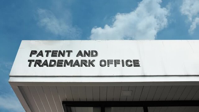 A Patent and Trademark Office word sign displayed on a governmental building under a clear blue sky, symbolizing intellectual property, innovation, legal registration, and protection