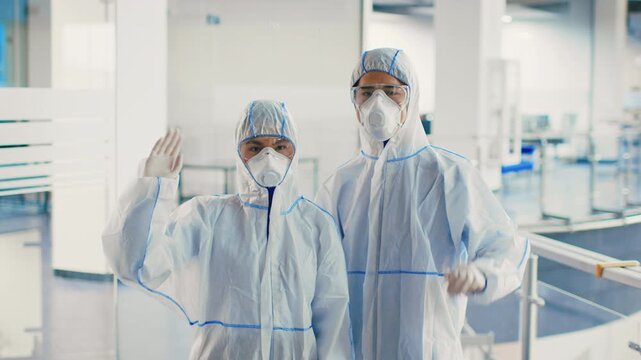 Two professionals in protective gear wave from a coworking space as they conduct disinfection efforts amid a pandemic. Their presence emphasizes workplace safety and hygiene efforts. - Powered by Adobe