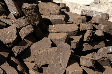 Dark coal bricks are piled high at a mining location under clear blue skies, showcasing their rough...