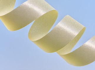 Elegant pearlescent paper ribbon with shimmer and texture in an abstract curve against a clean light blue background, ideal for luxury design.