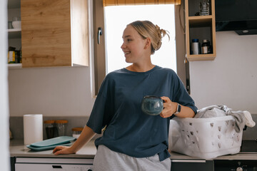 Laundry basket and coffee mug in a cozy home scene with a young woman in loungewear taking a break from housework; domestic life concept, candid indoor lifestyle background with copy space.