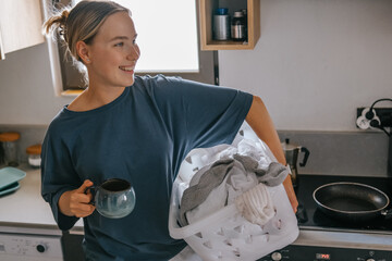 Laundry basket and coffee mug in a cozy home scene with a young woman in loungewear taking a break from housework; domestic life concept, candid indoor lifestyle background with copy space.