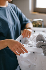 Laundry basket and coffee mug in a cozy home scene with a young woman in loungewear taking a break from housework; domestic life concept, candid indoor lifestyle background with copy space.
