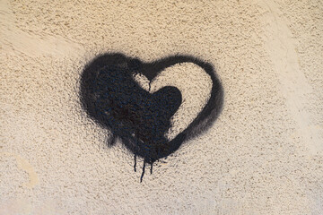 Black heart graffiti with dripping spray paint on textured beige wall, creating a raw street art aesthetic. Emotional background, rebellious urban expression, underground street art