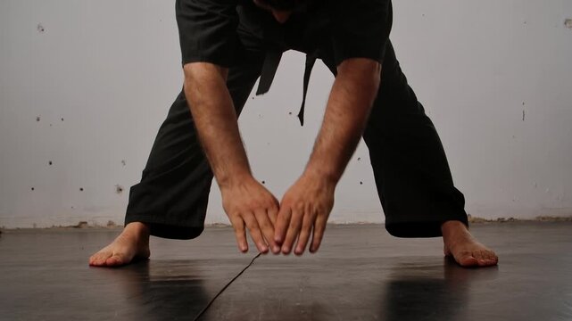Close up of the legs of a man practicing Wing Chun in a black kimono, demonstrating his skills against a gray studio backdrop, showing self defense training and martial arts techniques.