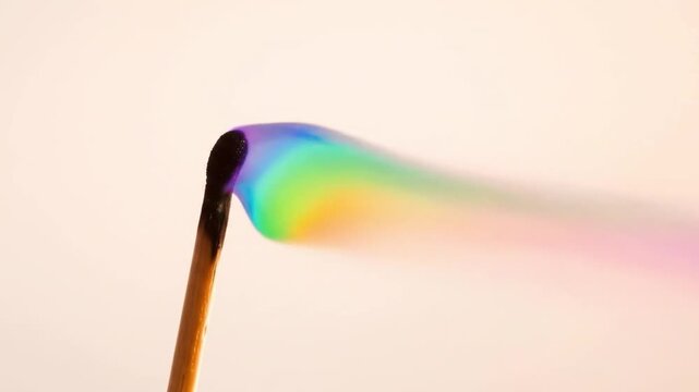 A burning matchstick emitting rainbowcolored smoke on a pale background