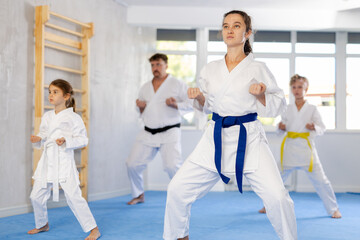Fototapeta premium Family with preteen children in kimono trying new martial moves at karate class