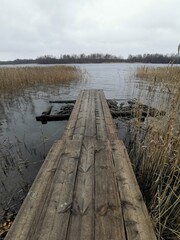 A rustic wooden walkway or pier extending into the calm, reed-lined water of Lake Onega on an overcast day, emphasizing tranquility and nature