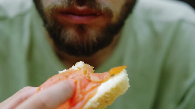 Close up of man taking a bite of sandwich with butter and red fish outdoors, showing natural lifestyle and casual food moment. 4k horizontal footage.