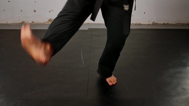 Close up of the legs of a man practicing Wing Chun in a black kimono, demonstrating his skills against a gray studio backdrop, showing self defense training and martial arts techniques.