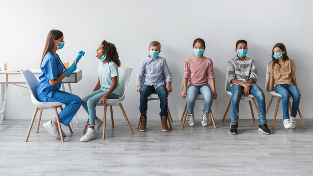 A medical worker conducts a coronavirus antigen test on a young girl while other children wait. The scene is set against a gray background, emphasizing the testing process. - Powered by Adobe