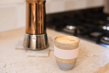 a flat white coffee in a pottery mug, with the copper moka pot  in the background