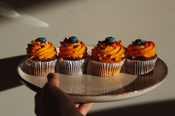 Delicious Halloween cupcake with orange frosting and blueberry held by a hand. A hand holds a cupcake with orange frosting, a blueberries