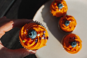 Delicious Halloween cupcake with orange frosting and blueberry held by a hand. A hand holds a cupcake with orange frosting, a blueberries