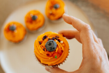 Delicious Halloween cupcake with orange frosting and blueberry held by a hand. A hand holds a cupcake with orange frosting, a blueberries