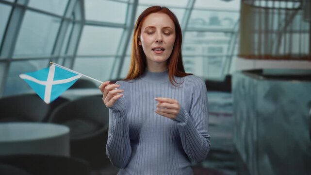 Woman with scottish flag in restaurant setting, showcasing nationality and culture indoors, with modern decor, emphasizing redhead beauty and elegant attire.