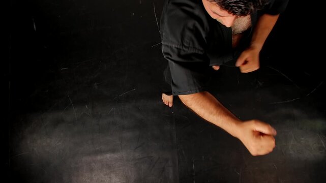 Top view of a man practicing Wing Chun in a black kimono, demonstrating hand control against a dark studio background, showing self defense training and martial arts techniques.